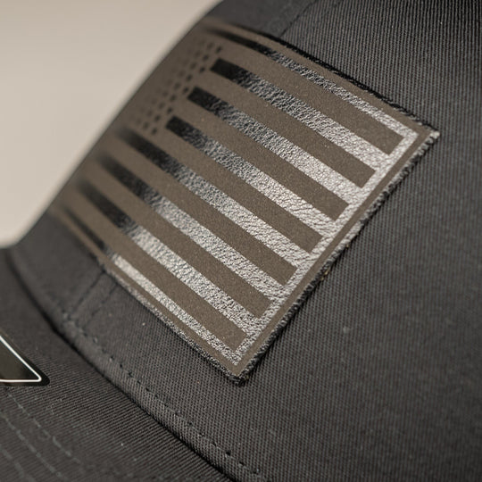 Single Track Hats black trucker cap with black leatherette USA flag patch. Adjustable snapback.